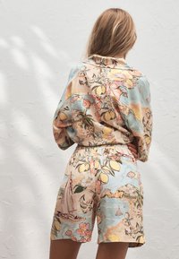 Mujer vista desde atrás con pantalones cortos a juego en tonos pastel y camisa de manga larga con estampado tropical y náutico.