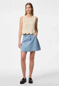 Crop top en tricot beige avec un motif ajouré et un ourlet festonné, associé à une jupe en denim A-line bleu clair et des mocassins noirs.