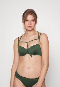 Conjunto de biquíni verde com um tecido texturizado, top estilo balconete com bordas onduladas, aros e múltiplas tiras finas com um detalhe central.