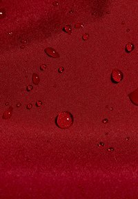 Des gouttes d'eau perlent sur un tissu rouge texturé, montrant une surface résistante à l'eau.
