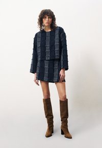 Marineblauw textuur tweedelig outfit met een geblokt patroon, lange mouwen en een mini-jurk. Gecombineerd met bruine kniehoge hakschoenen.