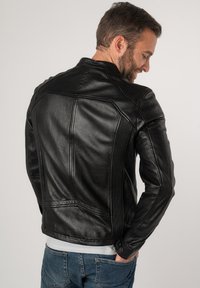 Schwarze Motorradlederjacke mit taillierter Passform, strukturierten Schultern und vertikalen Nähdetails. Getragen mit einem hellen Hemd.