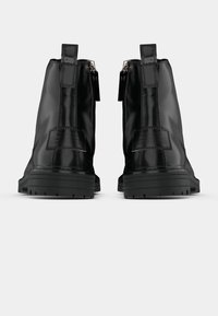 Črni sintetični gležnarji z okroglim prstom, stranskimi zadrgami in teksturiranimi obliži. Debel gumijast podplat z izrazitim profilom.