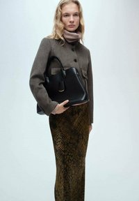 Schwarze Lederhandtasche mit strukturiertem Design und goldenen Akzenten, kombiniert mit einem braunen Wollmantel und einem grünen Schlangenlederrock für den Kontrast.