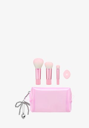 Tre makeupbørster med pink håndtag, en pink blender-svamp og en pink kosmetikpose med en sølv perlecharme og hjertenøglekæde.