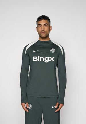Mørkegrøn langærmet træningstop med hvide accenter, der har Chelsea FC-logoet og "Bingx" trykt med fed hvid på fronten.