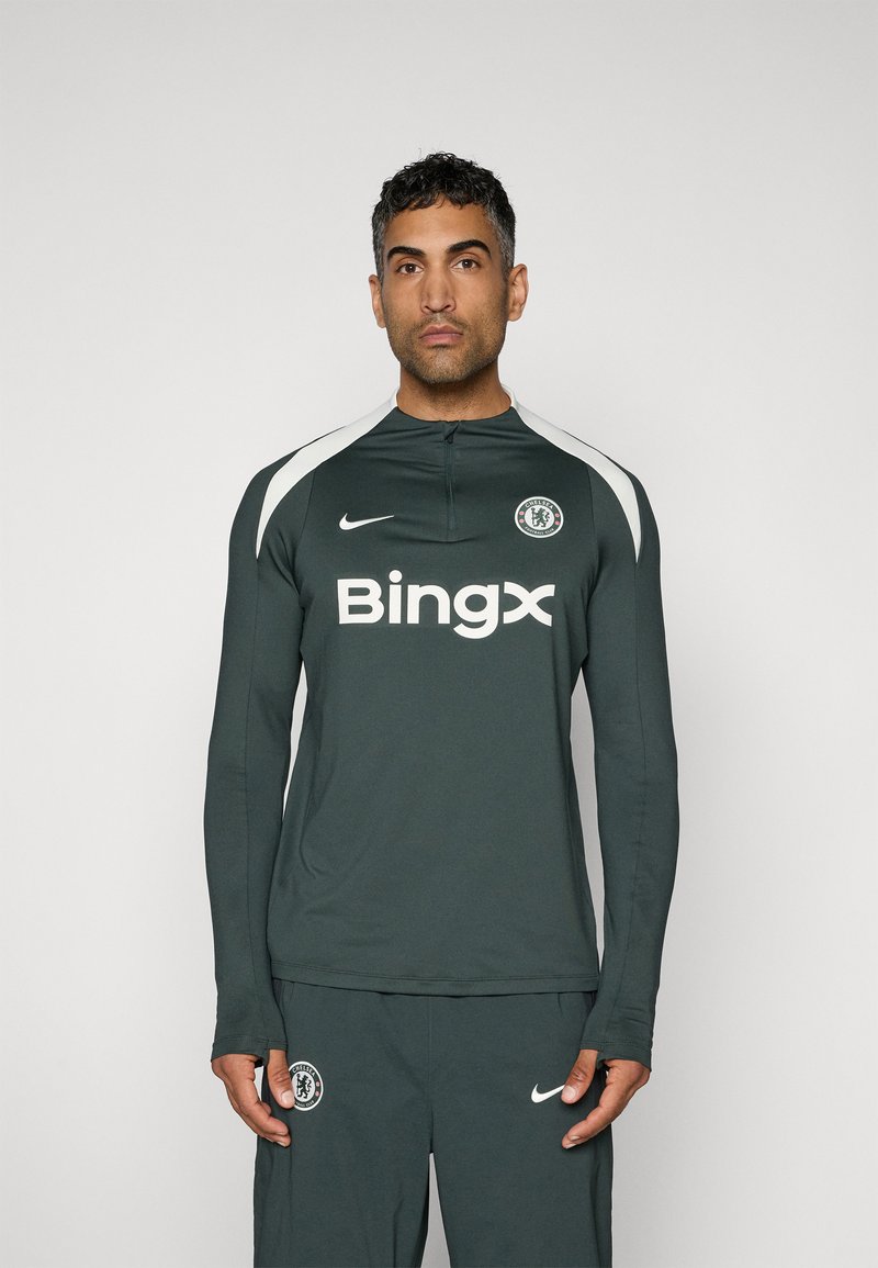 Tricou de antrenament cu mânecă lungă de culoare verde închis, cu accente albe, având logo-ul Chelsea FC și inscripția "Bingx" tipărită cu litere mari albe pe față.