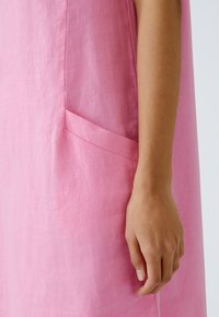 Rotes Leinenkleid mit Seitentasche; glatte Textur; das Design zeichnet sich durch eine lockere Passform und klare Linien mit minimalen Akzenten aus.