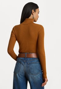 Rjava rebrasta turtleneck pulover, v kombinaciji z modrimi hlačami z visokim pasom, z rjavim pasom in zadnjimi žepi, prikazano s hrbtne strani.