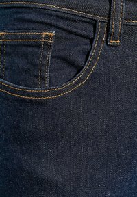 Ciemne dżinsy o klasycznym kroju, z pomarańczowymi szwami, tylną kieszenią oraz gładką, teksturowaną powierzchnią.