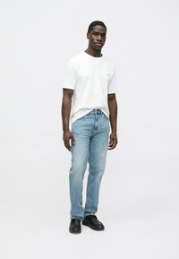 Balta kokvilnas T-krekls, gaiši zili džinsu bikses un melni apavi. Ikdienas stils ar taisnu bikšu kāju dizainu, uz krekla minimāla zīmola apdruka.