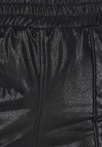 Zwarte stof met een metallic afwerking, met een glanzende, gekreukelde textuur en een elastische taille. Gladde oppervlakte met een lichte glans en plooien bij de tailleband.