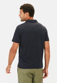 Marineblaues Poloshirt aus strukturiertem Stoff mit klassischem Kragen, kurzen Ärmeln und seitlichen Schlitzen, kombiniert mit hellgrünen Shorts.