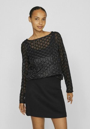 Black sheer top with diamond pattern and long sleeves, paired with a fitted black mini skirt. Textured fabric with subtle sheen.