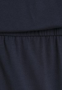 Marinblå bomullstyg med en slät textur, som har ett elastiskt midjeband i nederkant. Materialet är mjukt och något töjbart.