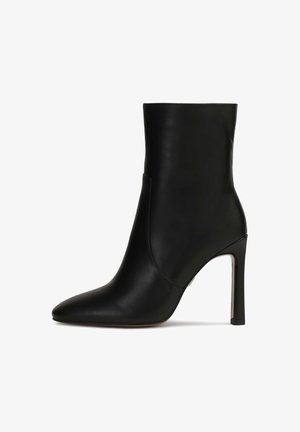 Czarna skórzana botka za kostkę z szpiczastym noskiem, wysokim obcasem typu stiletto i gładką teksturą. Charakteryzuje się eleganckim wzornictwem i minimalistycznymi detalami.
