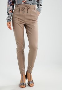 Beige, slim-fit broeken gemaakt van een glad materiaal, met een strik taille en zijzakken. Gecombineerd met sandalen met zilveren bandjes.