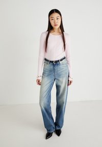 Haut à manches longues côtelé rose clair avec un col rond, associé à un jean droit bleu délavé et des escarpins noirs à talons pointus. Accents de bijoux simples.