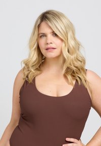 Brun ribbad linne med breda axelband och rundad halsringning. Modellen har axellång vågigt blont hår och en neutral bakgrund.