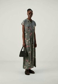 Μάξι φόρεμα σε πράσινο χρώμα με λουλουδάτο σχέδιο, κοντά μανίκια, ελαστική μέση και γιακά. Συμπληρώνεται με μαύρη τσάντα και σανδάλια.