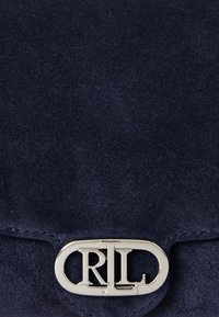 Marineblauwe suède clutch met een ovale zilverkleurige sluiting met de lettering 'CRL'. Zachte textuur, eenvoudig ontwerp en geen extra patronen.