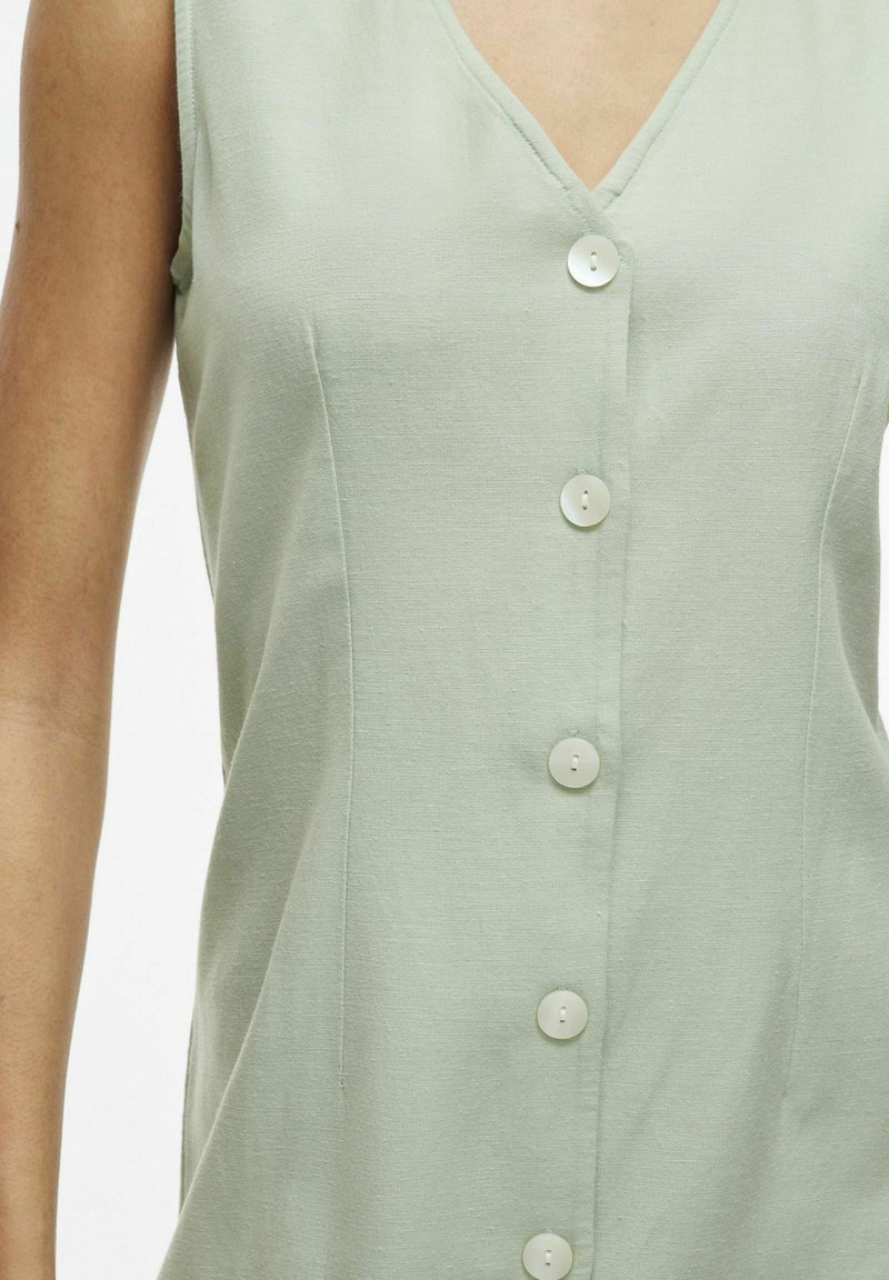 Robe sans manches vert clair avec un décolleté en V, dotée de six boutons ronds blancs sur le devant et d'un tissu doux et texturé.