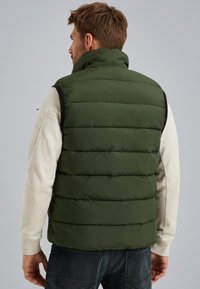 Green puffer vest with a high collar, featuring vertical quilted design, paired with a light gray long-sleeve shirt.