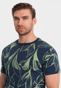 Marineblauwe t-shirt met korte mouwen en groen bladdessin. Gemaakt van katoen, met een ronde hals en een ontspannen pasvorm.