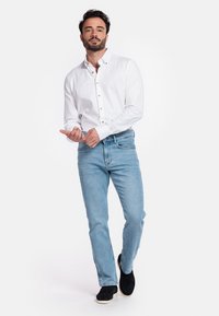 Witte overhemd met gouden knopen, lichtblauwe jeans en zwarte instappers, met een gladde textuur en een casual pasvorm.