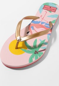 Rosa flip-flop med gyllene rem, med ett tropiskt mönster som har en flamingo, sol och palmer. Strukturen är med en slät fotbädd.