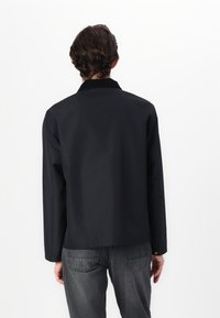 Black jacket with a collar, long sleeves, and straight cut. Made from smooth fabric, featuring minimal detailing and a classic design.