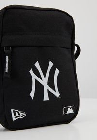 Borsa in tessuto nero con un grande logo bianco dei New York Yankees, dotata di chiusura con zip e ulteriore dettaglio del logo MLB bianco nella parte inferiore.