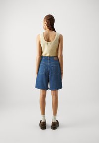 Débardeur en tricot beige clair avec des bords festonnés associé à un short en denim bleu taille haute. Présente deux poches arrière et une étiquette marron.