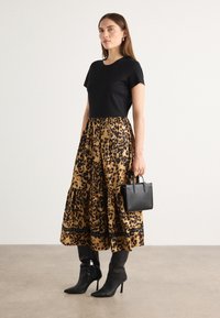 Top corto nero a maniche corte abbinato a una gonna a stampa leopardata con balze. Indossato con stivali neri con tacco a spillo e una piccola borsa nera.
