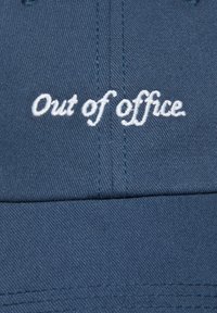 Niebieska czapka z bawełny z haftowanym na przedzie białym, okrągłym napisem "Out of office". Posiada wyszywane detale.