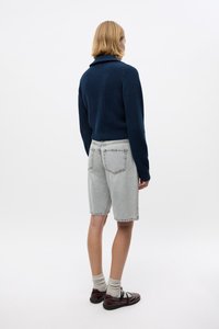 Jersey de punto azul marino con un cuello alto, combinado con pantalones cortos de mezclilla gris claro. El modelo lleva zapatos marrones y calcetines beige. Diseño simple.