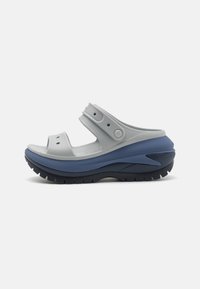 Ljusgrå sandal med justerbara remmar, strukturerad innersula, blå och mörkgrå plattform, med ventilationshål och en formad design.