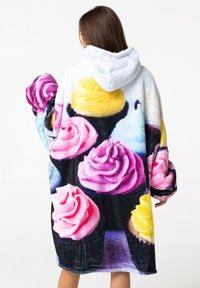 Manta con capucha con estampado de cupcakes en colores vibrantes, que presenta glaseado en rosa, púrpura y amarillo. Tejido suave y esponjoso con mangas sueltas.