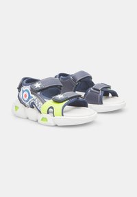 Sinine ja roheline laste sandaalid, millel on krõpsude rihmad, tekstuuriga kangas ja valge kummitald; sisaldavad tähe- ja sihtmärgi aktsente.