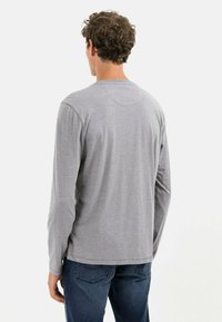 Grå langærmet skjorte med rund hals, lavet af blødt stof. Har et simpelt design og let buet kant. Båret med mørke jeans.