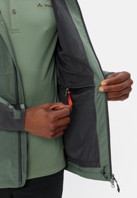 Green jacket with grey accents, zippered front and mesh lining. Notable details include an inner pocket with a red zipper pull.