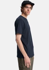 Camiseta de algodón azul marino con mangas cortas y cuello redondo, que presenta un sutil patrón moteado en toda su superficie.