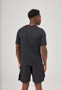 T-shirt de sport noir à manches courtes et encolure ronde, présentant un design sans couture et une texture lisse, associé à un short assorti.