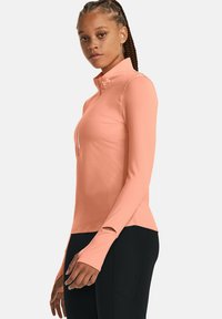 Pfirsichfarbenes langärmliges Sportshirt mit Reißverschluss am Hals, Daumenlöchern und taillierter Passform, hergestellt aus einem dehnbaren, atmungsaktiven Material.