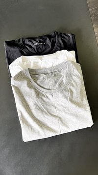 Tri kratke majice na kupu: črna na vrhu, bela v sredini, siva na dnu. Vsaka ima okroglo ovratnik in mehak bombažen material.