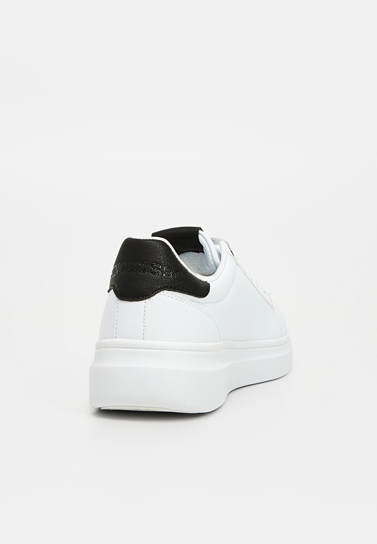 Baskets en cuir blanc avec un talon noir, présentant une texture lisse, une forme arrondie et une semelle en caoutchouc plate. Éléments de design minimalistes.