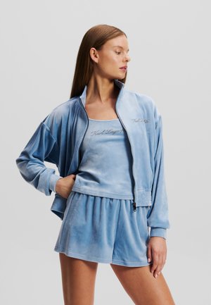 Light blue velour zip-up jacket with a high collar, paired with a matching sleeveless top and shorts. Features subtle brand embroidery.