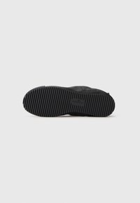 Schwarze Schuhsohle mit einer flachen, strukturierten Gummibeschichtung, die tiefe Rillen für besseren Halt aufweist. Minimalistisches Design mit eingeprägtem Markenlogo.