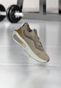 Beige Sport Schuh mit einer strukturierten Oberseite, flexiblem Profil und transparenten Details in der Zwischensohle. Merkmale sind Schnürsenkel und ein gepolsterter Schaft.