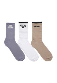 Trzy pary skarpetek w kolorze lawendowym, białym i beżowym, z kontrastującymi czarnymi ściągaczami. Każda skarpeta ma inny tekst: "NIE DZIŚ", "POPROWADŹ MNIE" oraz "NIE PANIKUJ".